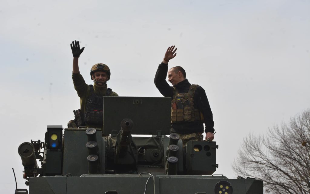 Двоє військових на військовій техніці махають руками у привітанні