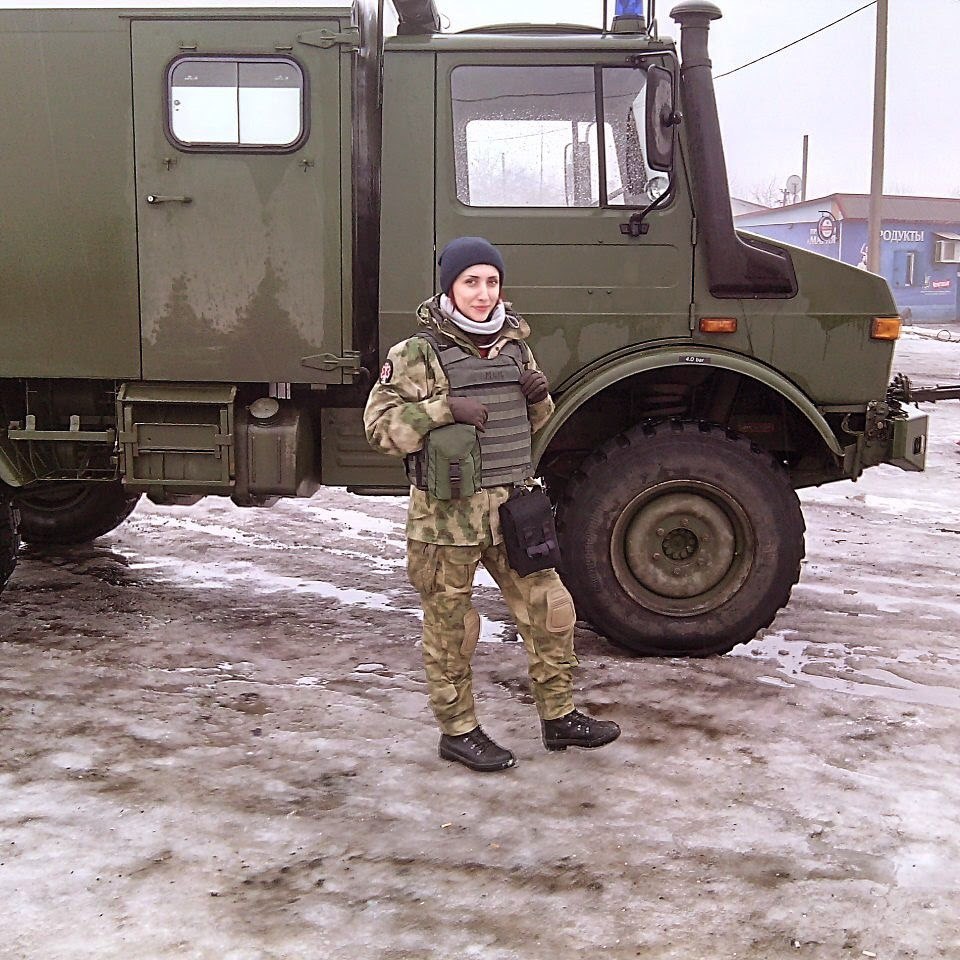 A woman in military uniform is posing in front of a military vehicle