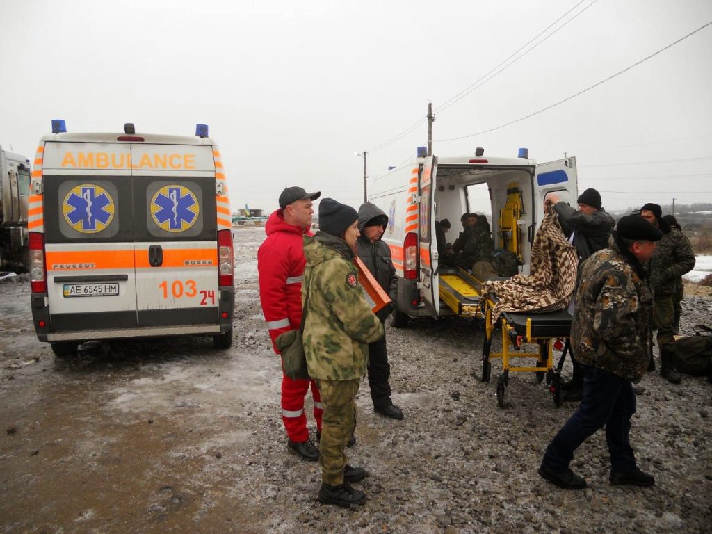 A group of people in medical and military uniforms is standing in front of two ambulances