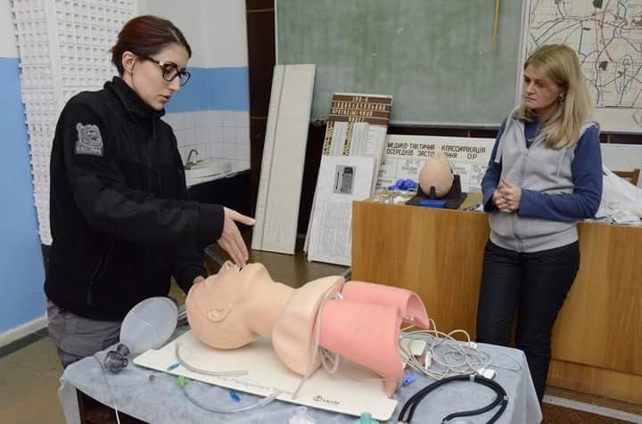 A tactical medicine instructor talks to a woman while using a medical mannequin