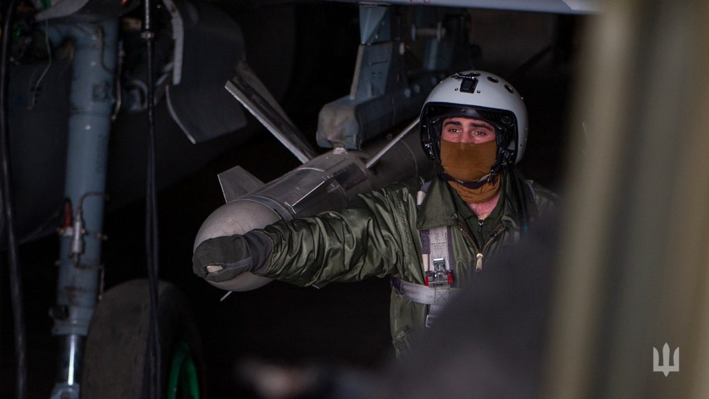 Чоловік у шоломі та військовій формі пілота поклав руку на боєприпас