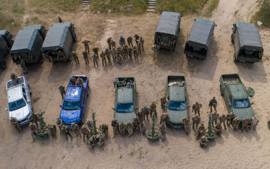 Група військових стоїть навколо пікапів та вантажівок