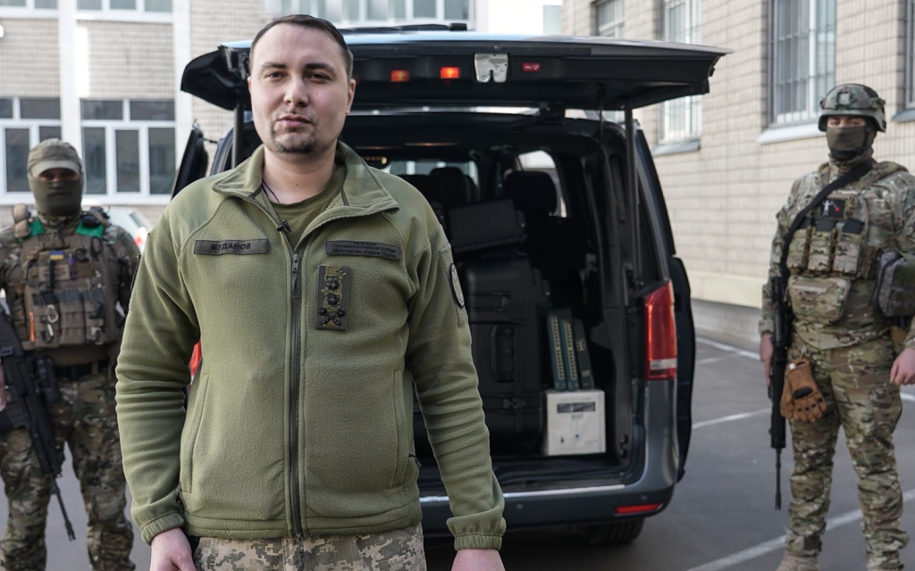 Генерал-майор Кирило Буданов стоїть перед відкритим капотом машини, позаду нього українські військовослужбовці із закритими обличчями