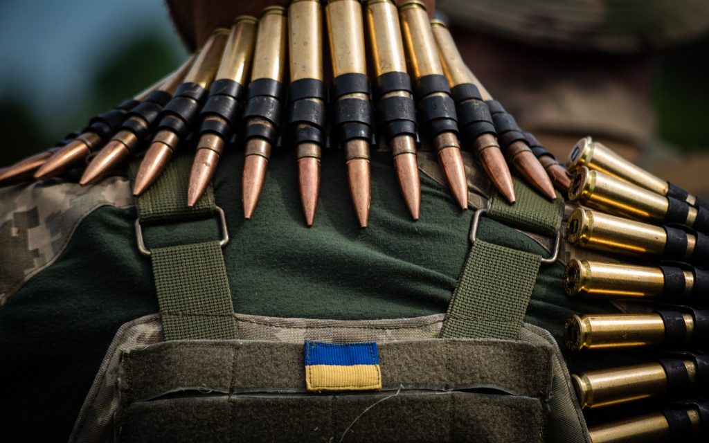 Стрічки з патронами висять на шиї і плечі українського військового під час навчання із загальної підготовки